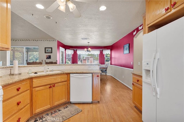 kitchen featuring a peninsula, a textured ceiling, a healthy amount of sunlight, light wood-type flooring, and white appliances