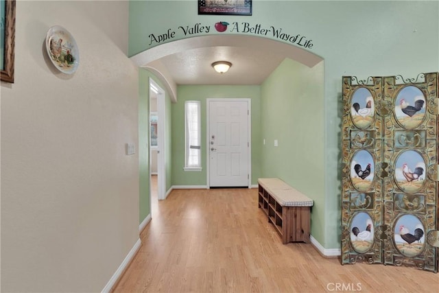 foyer entrance featuring baseboards, wood finished floors, and arched walkways