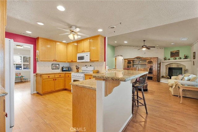kitchen with a ceiling fan, a textured ceiling, white appliances, light wood finished floors, and a peninsula