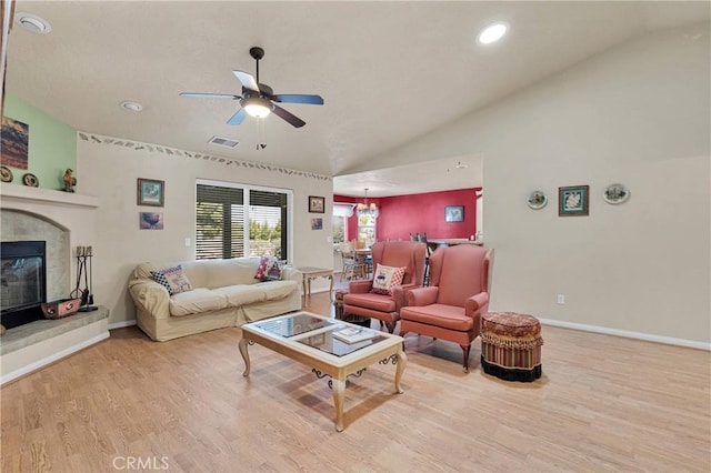 living area featuring lofted ceiling, wood finished floors, a tiled fireplace, and a ceiling fan