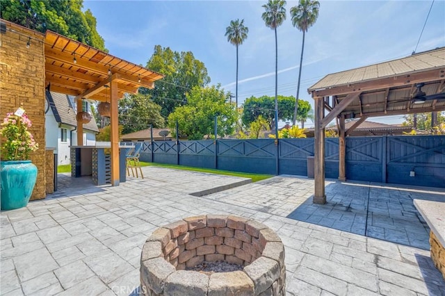 view of patio featuring a gate, outdoor dry bar, fence, ceiling fan, and a fire pit