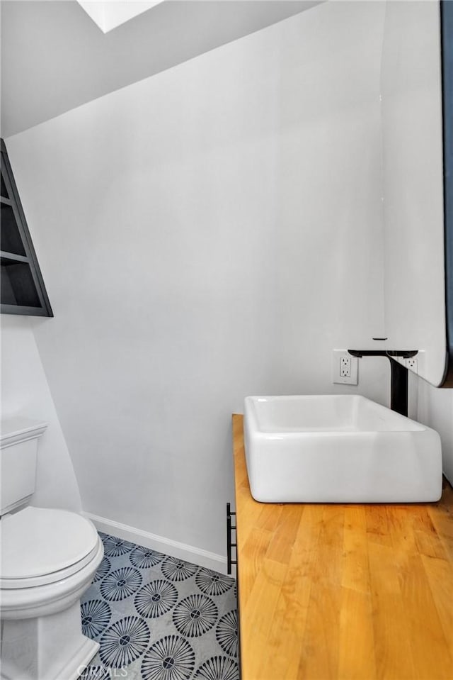 bathroom featuring tile patterned floors, toilet, a sink, a skylight, and baseboards