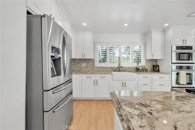 kitchen featuring backsplash, appliances with stainless steel finishes, white cabinetry, and a sink