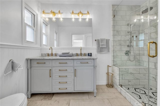 bathroom with a shower stall, toilet, a wainscoted wall, and a sink