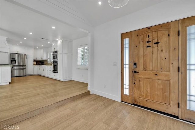 entrance foyer featuring recessed lighting, light wood-style flooring, lofted ceiling, and baseboards