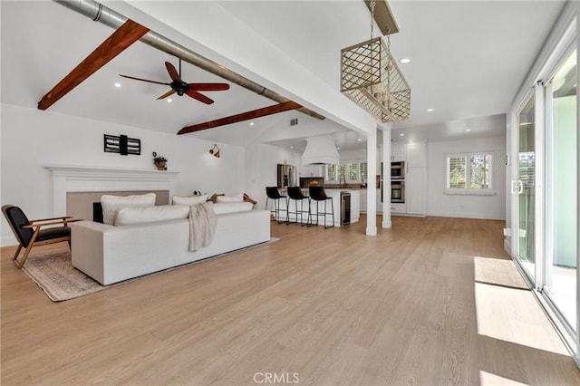 living area featuring a ceiling fan, vaulted ceiling with beams, light wood-style flooring, a fireplace, and recessed lighting