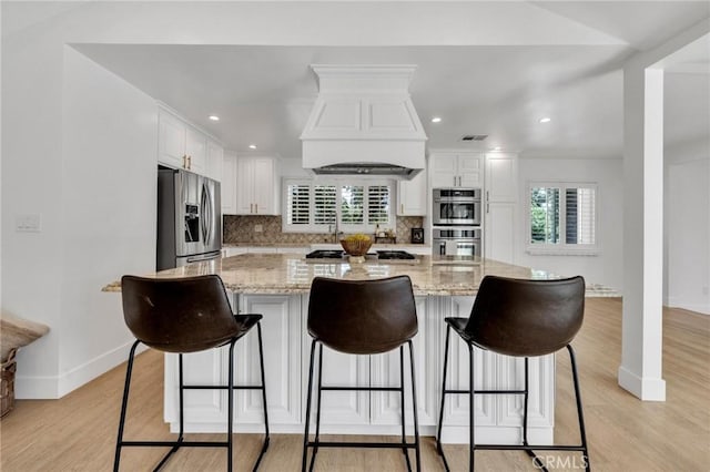 kitchen featuring a healthy amount of sunlight, white cabinetry, custom range hood, baseboards, and appliances with stainless steel finishes