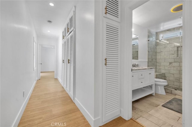 corridor with baseboards, recessed lighting, light wood-style floors, and a sink