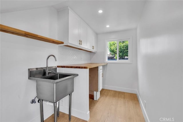 kitchen featuring butcher block countertops, light wood-style floors, white cabinets, baseboards, and recessed lighting