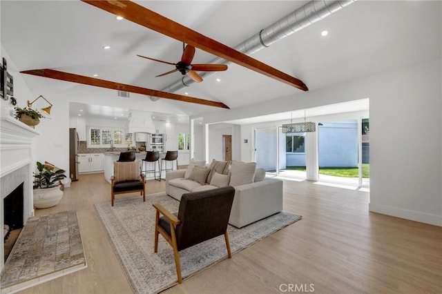 living room featuring a fireplace, light wood finished floors, vaulted ceiling with beams, and ceiling fan