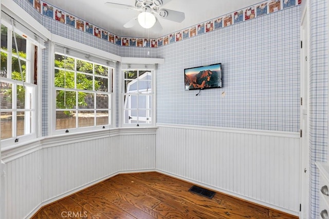 empty room featuring wood finished floors, a ceiling fan, visible vents, and a wainscoted wall