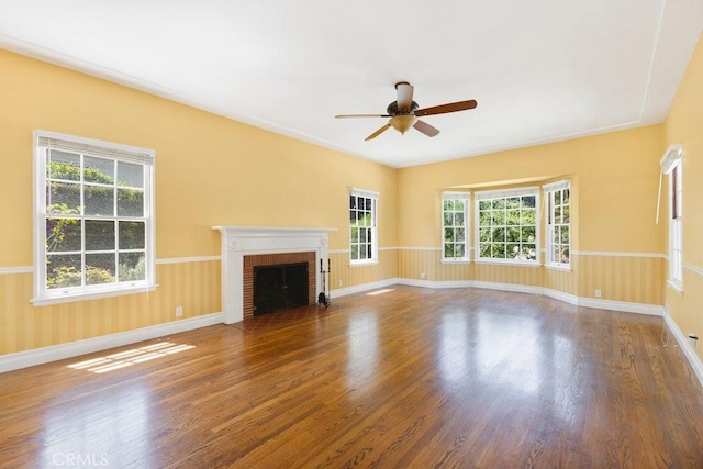 unfurnished living room with wood finished floors, a brick fireplace, a ceiling fan, and baseboards