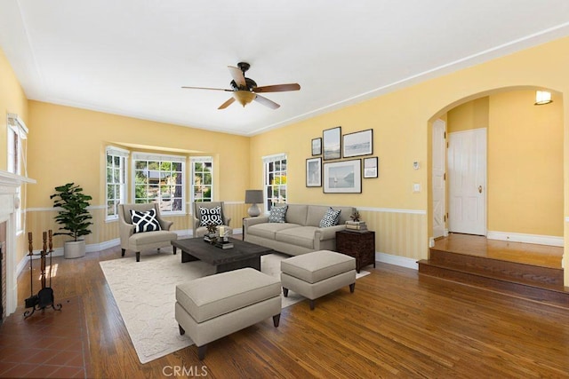 living room with a ceiling fan, a fireplace with flush hearth, arched walkways, dark wood finished floors, and baseboards