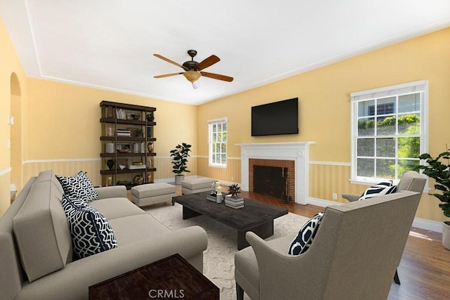 living room featuring a fireplace, wood finished floors, arched walkways, and a ceiling fan