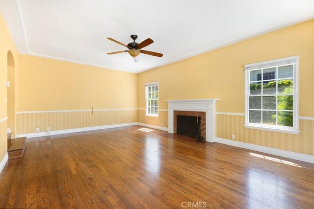 unfurnished living room with wood finished floors, ceiling fan, arched walkways, a fireplace, and baseboards
