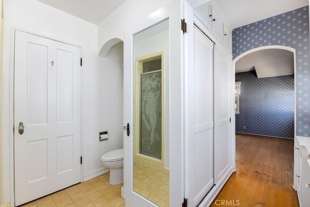 full bath featuring wallpapered walls, wood finished floors, toilet, and a stall shower