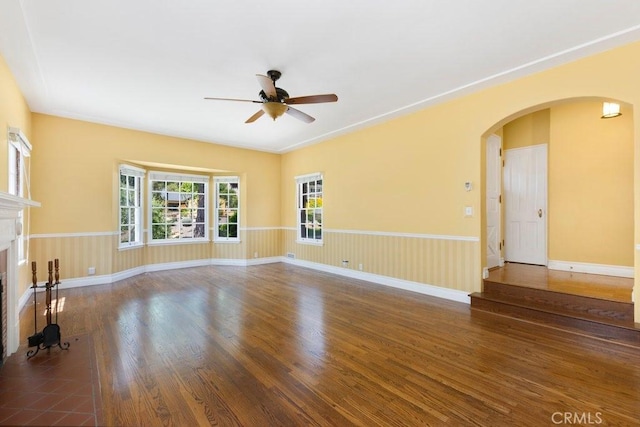 unfurnished living room with arched walkways, baseboards, wood finished floors, ceiling fan, and a fireplace