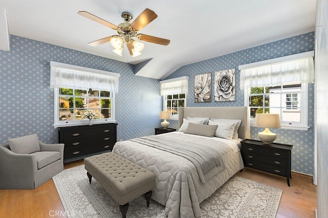 bedroom with wallpapered walls, vaulted ceiling, wood finished floors, and ceiling fan