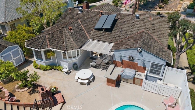 rear view of property with a chimney, roof mounted solar panels, fence, an outbuilding, and a patio