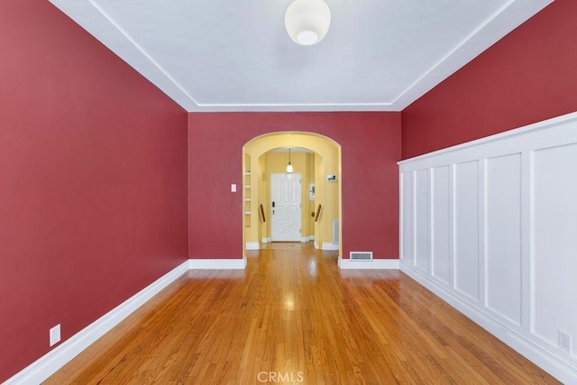 spare room with arched walkways, wood finished floors, visible vents, and baseboards
