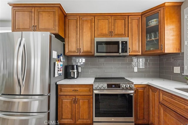 114 Via Estrada Unit B, Laguna Woods, CA 92637 - kitchen with backsplash, brown cabinetry, appliances with stainless steel finishes, and glass insert cabinets