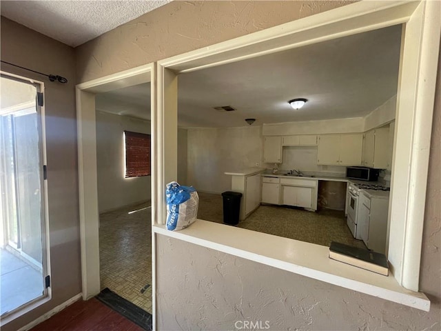 kitchen with a sink, white range with gas stovetop, light countertops, stainless steel microwave, and visible vents