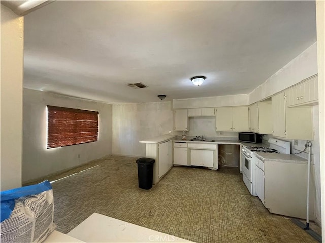 kitchen featuring stainless steel microwave, light countertops, white gas range oven, and a sink