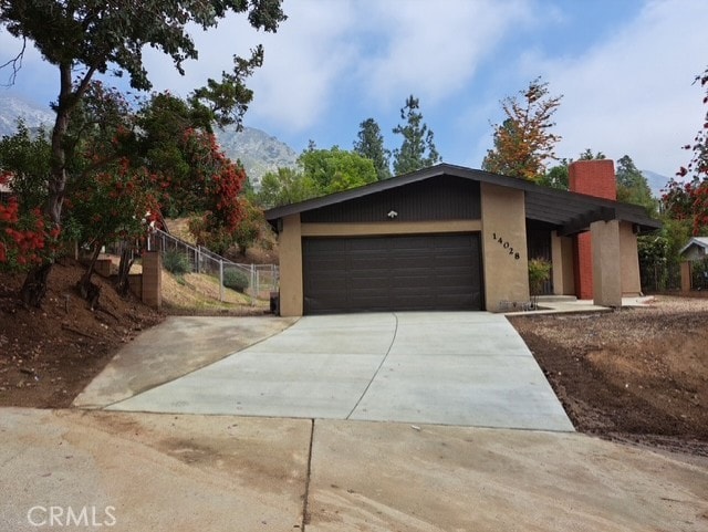 view of front of home with fence, an attached garage, stucco siding, a chimney, and concrete driveway