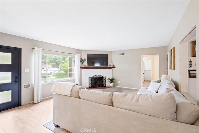 living room featuring baseboards, a fireplace, light wood finished floors, and visible vents