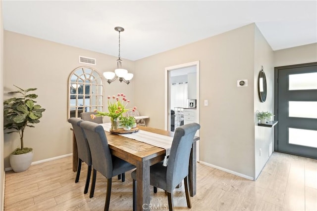 dining space featuring baseboards, light wood-style flooring, a chandelier, and visible vents