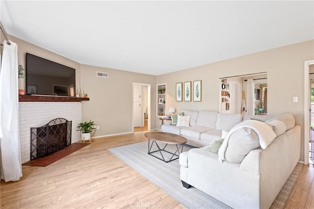 living area with visible vents, baseboards, a brick fireplace, and wood finished floors