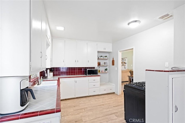 kitchen with white cabinets, black range with gas stovetop, tile countertops, stainless steel microwave, and visible vents