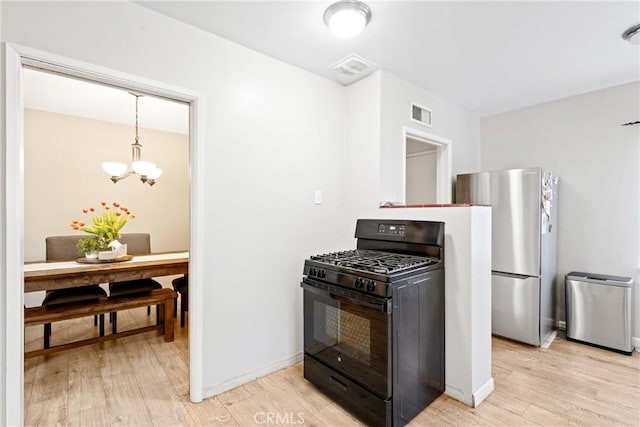 kitchen featuring black gas range, freestanding refrigerator, visible vents, an inviting chandelier, and light wood-style floors
