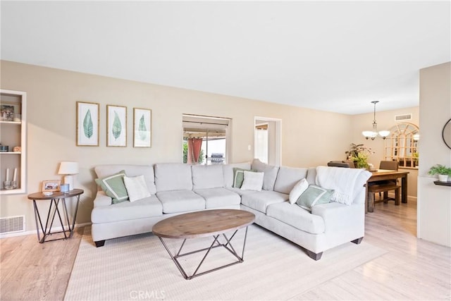 living area featuring a chandelier, baseboards, visible vents, and light wood finished floors