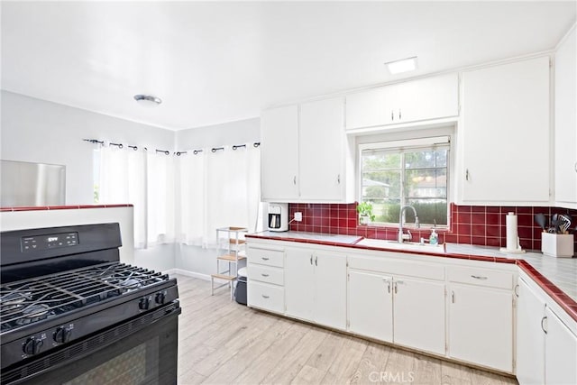 kitchen featuring black gas stove, a sink, tile countertops, and tasteful backsplash