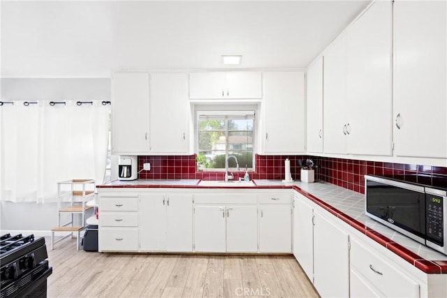 kitchen featuring tile counters, white cabinetry, stainless steel microwave, a sink, and gas stove