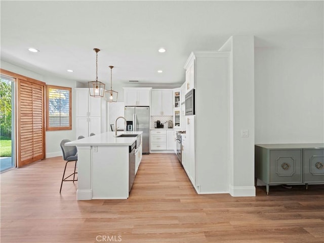 25626 Moore Ln, Stevenson Ranch, CA 91381 - kitchen featuring appliances with stainless steel finishes, a kitchen bar, white cabinets, backsplash, and light wood finished floors