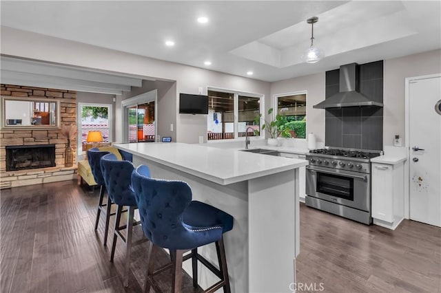 kitchen with high end range, wall chimney exhaust hood, a breakfast bar, a stone fireplace, and light countertops