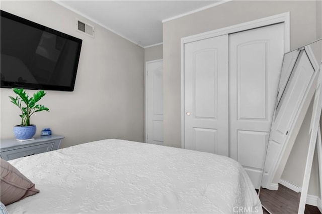 bedroom with wood finished floors, a closet, baseboards, visible vents, and crown molding