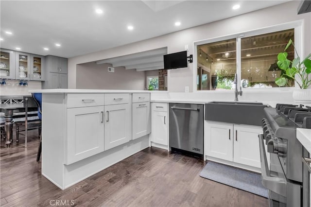 kitchen with glass insert cabinets, stainless steel appliances, light countertops, a sink, and a peninsula