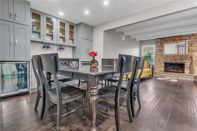dining area with a bar, visible vents, a stone fireplace, beverage cooler, and dark wood finished floors