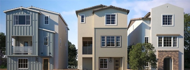 view of front facade featuring board and batten siding, brick siding, a balcony, and stucco siding
