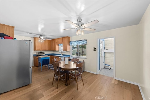 dining area with light wood finished floors, a ceiling fan, and baseboards