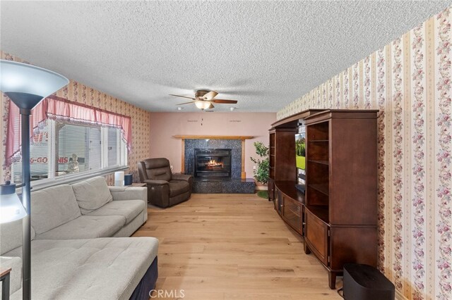 living area featuring wallpapered walls, light wood-style flooring, a textured ceiling, and a ceiling fan