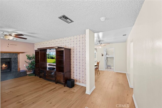 living room featuring a textured ceiling, light wood-style flooring, visible vents, and ceiling fan