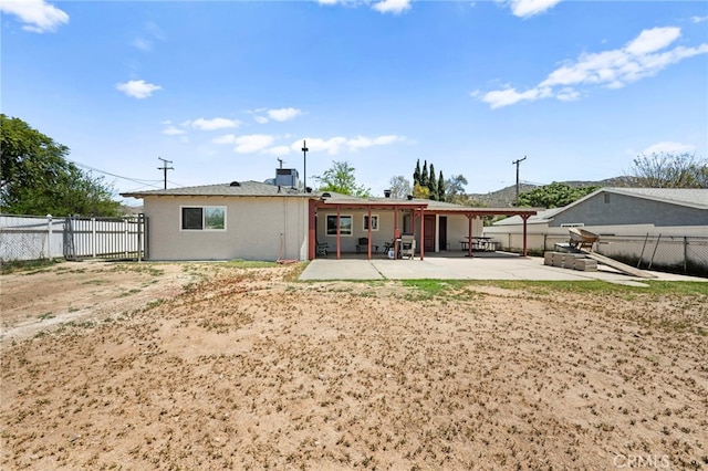 rear view of house with stucco siding, a fenced backyard, and a patio