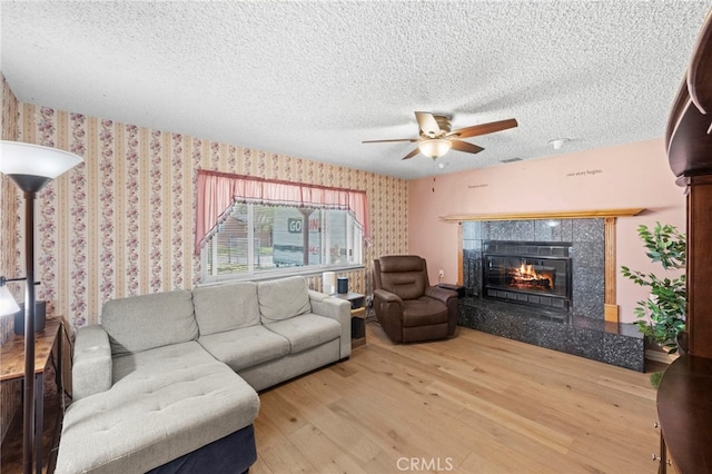 living room featuring ceiling fan, wood finished floors, a textured ceiling, and a tiled fireplace