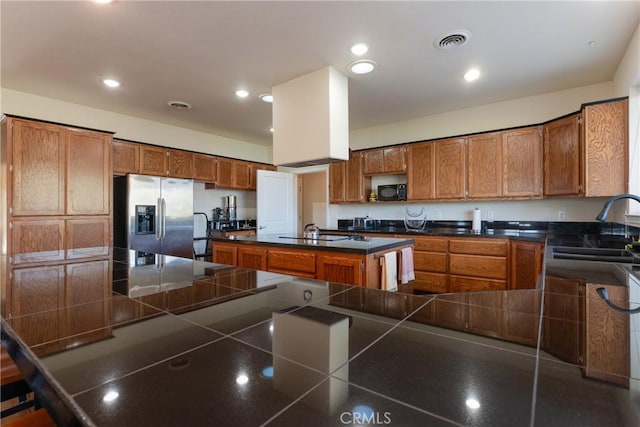 kitchen with dark countertops, a sink, brown cabinets, stainless steel fridge, and visible vents