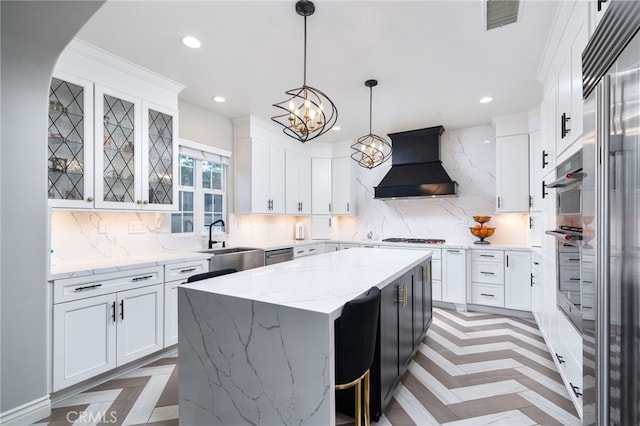 kitchen with backsplash, visible vents, a sink, a kitchen island, and custom exhaust hood