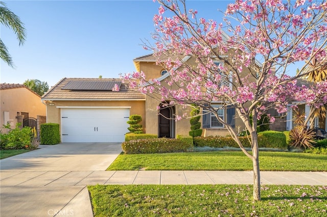 view of front of house featuring solar panels, driveway, an attached garage, a front yard, and stucco siding
